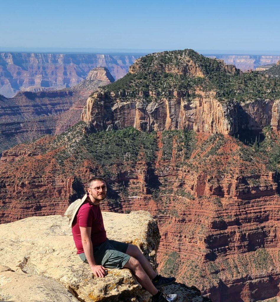 Photography of Paweł Swaczyna sitting on rock with the Grand Canyon in the background.